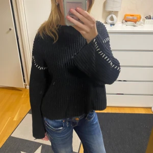 Svart stickad tröja med vita detaljer - Säljer en svart stickad tröja med vita sömdetaljer på ärmarna. Tröjan har en lös passform och långa ärmar, perfekt för kyligare dagar. OBS! Spegeln som är smutsig!!!!💗💗💗💗sååå snygg!!!