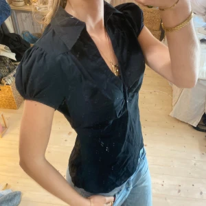 Svart kortärmad blus - Snygg svart blus med korta ärmar och knappar framtill. Den har en klassisk krage och en figurnära passform som ger en elegant look. Perfekt för att klä upp en vardagsoutfit eller för en mer formell stil💕💕