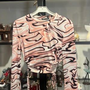 Mönstrad långärmad topp från Shein - Trendig långärmad topp från Shein med ett abstrakt mönster i rosa, svart och vitt. Toppen har knytband i midjan för en justerbar passform. Perfekt för att ge en färgglad touch till din outfit.