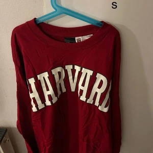 Vinröd tröja med Harvard-tryck - Snygg vinröd tröja med stort Harvard-tryck i vitt på framsidan. Perfekt för en avslappnad stil med en touch av college-vibe. Rund halsringning och långa ärmar gör den bekväm och lätt att bära.