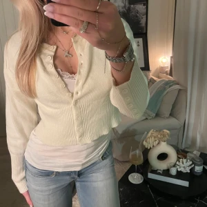 Vit ribbad kofta - Säljer en stilren vit ribbad kofta med knappar framtill. Koftan har långa ärmar och en croppad passform, perfekt för lager-på-lager-stil. Passar bra till både jeans och kjol.