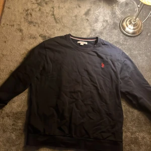 Svart tröja från U.S. Polo Assn. - Säljer en stilren svart tröja från U.S. Polo Assn. med röd broderad logga på bröstet. Tröjan har långa ärmar och rund halsringning. Perfekt för en avslappnad look. Den e äkta vill bara bli av med den 
