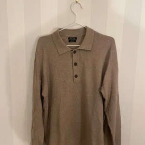 Beige pikétröja från Massimo Dutti - Snygg beige pikétröja från Massimo Dutti med långa ärmar och tre knappar framtill. Perfekt för en stilren och avslappnad look. Väldigt skön och mjuk material. Tveka inte att hojta till vid eventuella frågor!