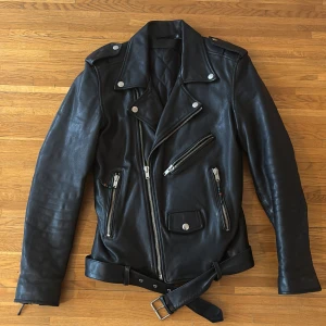 Svart skinnjacka från BLK DNM - Snygg svart skinnjacka från BLK DNM med klassisk bikerstil. Jackan har flera dragkedjor och en bälte i midjan för en cool look. Perfekt för att ge din outfit en edgy touch.