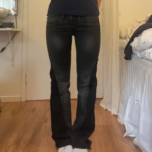 Svarta bootcut jeans - Snygga svarta/gråa lågmidjade bootcut jeans. Jag är 167 cm lång. Jeansen är utsydda. De är lite trasiga (se bild) men i övrig gott skick