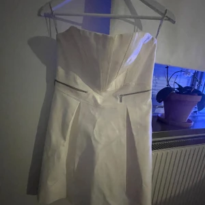 Vit axelbandslös klänning från Karen Millen - Elegant vit axelbandslös klänning från Karen Millen med dragkedjedetaljer i midjan. Perfekt för en fin look.Priset kan diskuteras.