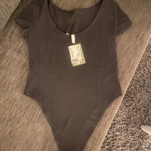 Svart kortärmad bodysuit - Säljer en stilren svart bodysuit med korta ärmar och rund urringning bak till. Den har knäppning i grenen. 