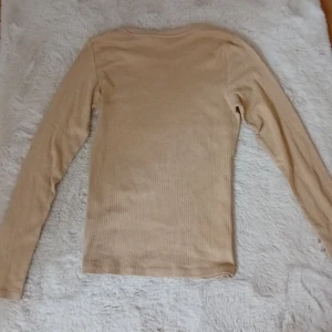 Beige ribbad långärmad tröja - Säljer en stilren beige ribbad tröja med långa ärmar. Perfekt för en avslappnad och bekväm look. Passar bra till både jeans och kjol.