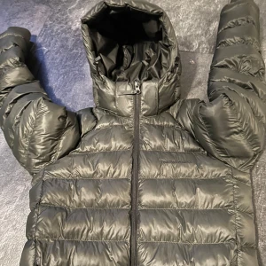 Svart pufferjacka från Peak Performance - Säljer en grön pufferjacka från Peak Performance. Jackan har en praktisk dragkedja och en mysig huva för extra värme. Perfekt för kyliga dagar.