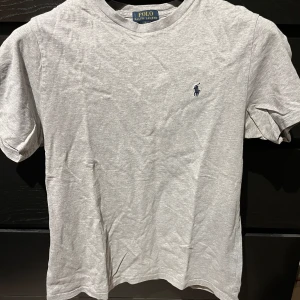 Grå t-shirt från Polo Ralph Lauren - Säljer en klassisk grå t-shirt från Polo Ralph Lauren med korta ärmar och det ikoniska broderade logotypen på bröstet. Perfekt för en avslappnad stil. Inköpt från Kidsbrandstore och är i barnstorlek L 14-16 år. Vilket motsvarar S i herrstorlek enligt mig. 