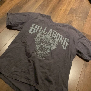 Grå t-shirt från Billabong - Säljer en grå t-shirt från Billabong med ett stort tryck på framsidan. Perfekt för en avslappnad stil. Märket är känt för sin surfkultur och design från Australien.