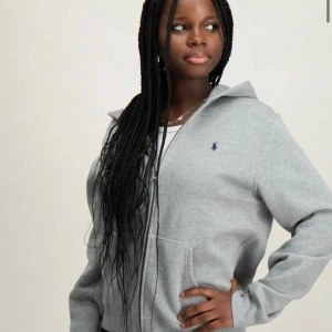 Grå hoodie från Ralph Lauren - Säljer en stilren grå hoodie från Ralph Lauren med dragkedja och det klassiska logotypbroderiet på bröstet. Perfekt för en avslappnad look. Hoodien har långa ärmar och en bekväm passform. STORLEK L I BARN STORLEK (passar Xs/Xxs)