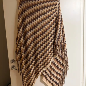 Mönstrad halsduk med fransar - Snygg halsduk med zigzag-mönster i beige, brun och svart. Den har fransar längs kanterna och är perfekt för att ge en bohemisk touch till din outfit. Passar bra till kyligare dagar.