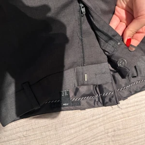 grå kostymbyxor med dragkedja lågmidjade - Snygga grå  kostymbyxor med dragkedja och knappstängning. Byxorna har en klassisk design med raka ben och diskreta fickor baktill. Perfekta för en stilren look. Lågmidjade. Passar mig perfekt längdmässigt som är 169 cm lång. 