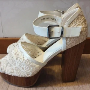 Vita spetsiga sandaler med träklack - Snygga vita sandaler med spetsdetaljer och hög träklack. De har en justerbar rem med spänne runt ankeln för extra stöd. Perfekta för en somrig look.