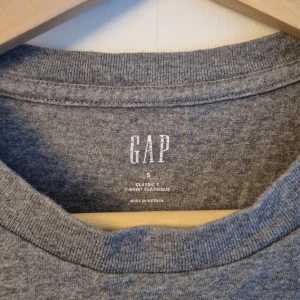 Grå t-shirt från GAP - Klassisk grå t-shirt från GAP i storlek S. T-shirten är kortärmad och tillverkad av bomull.