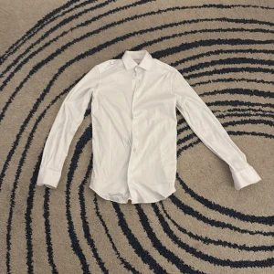 Vit skjorta från Massimo Dutti - Säljer en stilren vit skjorta från Massimo Dutti i herrstorlek S. Skjortan har långa ärmar och knappar framtill. Perfekt för en elegant look. Längst ut vid handleden har den pyttelite rosa på innersidan, ungefär en centimeter. Detta syns inte och man märker inte av det om man inte inspekterar noga, skriv vid minsta fundering!