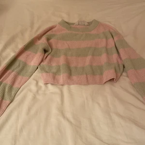 Randig croppad tröja från H&M - Säljer en söt randig tröja från H&M i rosa och grön. Tröjan är croppad och har långa ärmar med ribbade muddar. Perfekt för en avslappnad stil.