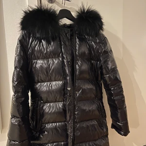 Svart dunjacka med pälskrage - Snygg svart dunjacka med glansigt material och en fluffig pälskrage. Jackan har långa ärmar och stängs med dragkedja. Perfekt för kalla vinterdagar. Feminina of sweden jacka pris går o diskuteras vid snabb affär inget fel på den 
