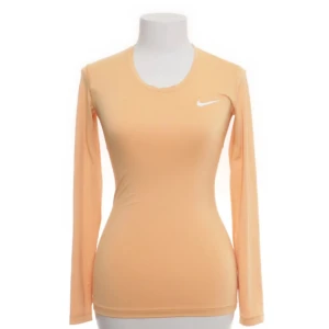 Persikofärgad långärmad topp från Nike - Säljer en persikofärgad långärmad topp från Nike med Dri-Fit-teknologi. Perfekt för träning med sin tighta passform och bekväma material. Den har en liten vit Nike-logga på bröstet. Passar utmärkt för aktiva dagar!