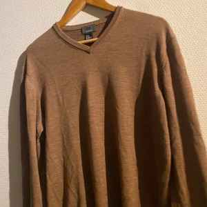 Brun tröja i merinoull från H&M - Säljer en stilren brun tröja i mjuk merinoull från H&M. Tröjan har en v-ringad hals och långa ärmar, perfekt för kyligare dagar. Passar bra till både vardag och mer uppklädda tillfällen. Passformen är true to size!