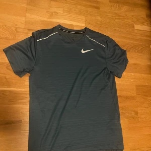 Mörkblå Dri-FIT t-shirt från Nike storlek S - Säljer en mörkblå Dri-FIT t-shirt från Nike, perfekt för löpning. T-shirten har korta ärmar och en liten vit Nike-logga på bröstet. Materialet är lätt och andas bra, vilket gör den idealisk för träning. Storlek S