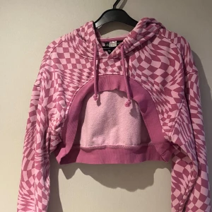 Rosa och vit mönstrad croppad hoodie - Säljer en cool rosa och vit mönstrad croppad hoodie med långa ärmar och justerbar huva. Perfekt för en avslappnad stil med en twist. Mönstret ger en unik look som sticker ut.