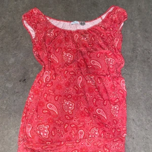 Röd mönstrad blus - Säljer en röd blus med paisleymönster. Blusen har korta ärmar och en rund halsringning. Perfekt för en färgglad och bekväm stil.