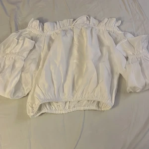 Vit offshoulder topp från Gina Tricot - Säljer en söt vit offshoulder topp från Gina Tricot. Toppen har elastiska detaljer vid ärmar och midja för en bekväm passform. Perfekt för varma dagar. Aldrig använd så den är som ny men eftersom lappen inte är kvar säljs den billigt. Storlek S. Från Gina Tricot.