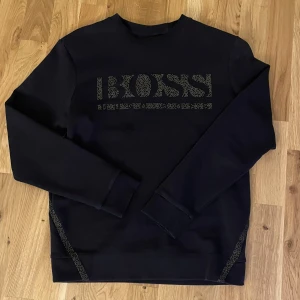 Svart hugo boss tröja - Snygg svart tröja från Boss med ett stilrent mönster på framsidan. Tröjan har långa ärmar och en bekväm passform. Perfekt för en avslappnad stil. Perfekt skick, använd fåtal gånger. Hör gärna av er:)