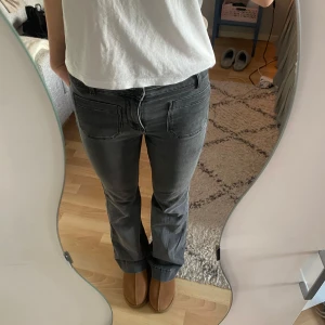 Grå bootcut jeans - Snygga grå bootcut jeans med en cool broderad detalj på bakfickan. De har en klassisk femficksdesign och är perfekta för en avslappnad stil. Passar bra till både sneakers och boots. Passar mig som är 177 cm! 