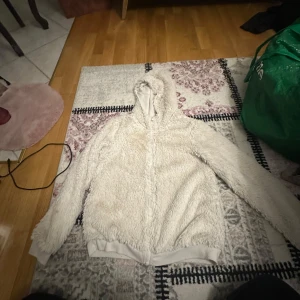 Vit  teddyjacka från Kappahl - Mysig beige teddyjacka från Kappahl med huva och dragkedja. Perfekt för kyliga dagar när du vill hålla dig varm och bekväm. Jackan har en fluffig yta som ger en trendig look.