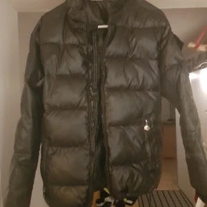 Svart pufferjacka - Snygg svart pufferjacka med dragkedja framtill. Jackan har en quiltad design och långa ärmar, perfekt för kyligare dagar. Praktiska fickor med dragkedja på sidorna.