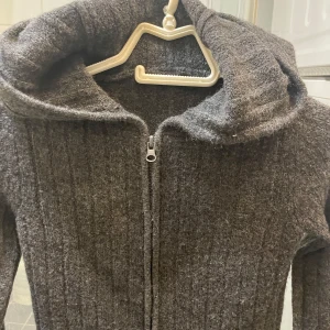 Kofta - Säljer en mysig grå ribbad hoodie från 157. Den har en dragkedja framtill och en stor huva för extra komfort. Perfekt för kyliga dagar!