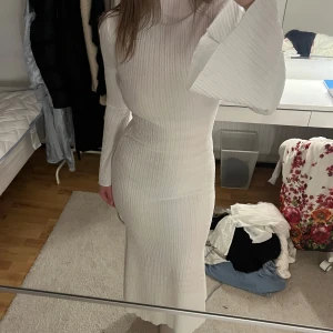 Vit ribbad långklänning - Elegant vit ribbad långklänning med långa ärmar och utsvängda ärmslut. Perfekt för en stilren och sofistikerad look. Modest!