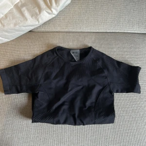 Svart kortärmad topp från Aim'n - Snygg svart topp från Aim'n med korta ärmar och en sportig design. Perfekt för träning eller en avslappnad dag. Den har en diskret logga på sidan och är tillverkad i ett bekvämt material.