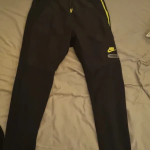  Nike byxor - Snygga svarta träningsbyxor från Nike med gul logga och detaljer. Byxorna har en tight passform och är perfekta för träning. De har en elastisk midja för extra komfort.