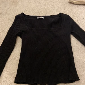 Svart ribbad topp från Zara - Snygg svart ribbad topp från Zara med långärmad design. Perfekt för en stilren look. Toppen har en fyrkantig halsringning som ger en modern touch.
