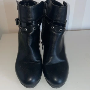 Svarta boots med klack och bälte Renato Balestra  - Snygga svarta italienska stövletter Renato Balestra med klack och dekorativt bälte runt ankeln. Skorna har en dragkedja på sidan för enkel på- och avtagning. Perfekta för en stilren look.