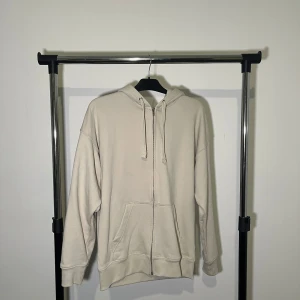 Beige hoodie från H&M - Säljer en stilren beige hoodie från H&M i storlek M. Den har en dragkedja framtill och en praktisk känguruficka. Perfekt för en avslappnad look.