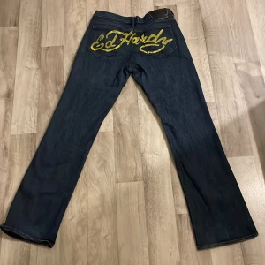 Lågmidjade jeans från Ed Hardy - Lågmidjade jeans från Ed Hardy med gult tryck baktill och broderi på framfickan. Jeansen har en straight passform och mycket stretch. Väldigt sköna! Jeansen är i superfint skick! Priset kan såklart diskuteras💕