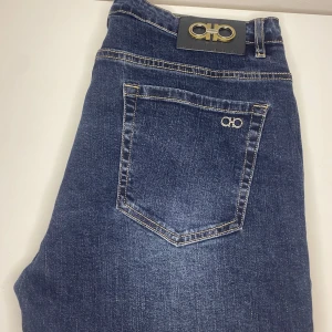 Ferragamo jeans  - Snygga blå jeans med stilrena logotypdetaljer på både knapp och bakficka. Byxorna har en klassisk femficksdesign och kontrastsömmar som ger en cool look. Perfekta för en avslappnad stil.                      Stories 36  
