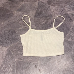 Vit ribbad linnetopp - Säljer en vit ribbad linnetopp med smala axelband. Perfekt för varma dagar eller som ett lager under andra plagg. Enkel och stilren design.