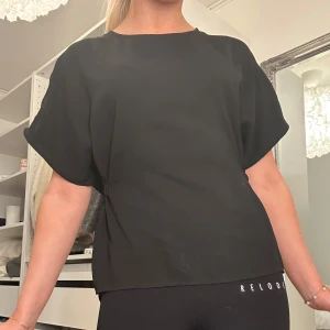 Svart topp med knytband - Säljer en stilren svart topp med korta ärmar och knytband i ryggen. Perfekt för en avslappnad men chic look. Toppen har en lös passform och är tillverkad i ett mjukt material.