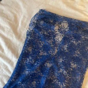 Blått spetlinne som är v ringat - Säljer en elegant blå spetsklänning med ett vackert blommigt mönster. Klänningen är perfekt för speciella tillfällen och har en stilren design som framhäver detaljerna i spetsen.