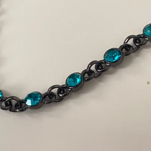 Armband med turkosa stenar - Snyggt armband med turkosa stenar infattade i en mörk kedja. Perfekt för att ge en färgklick till din outfit. Armbandet har en justerbar kedja för att passa olika storlekar. 17-21 cm