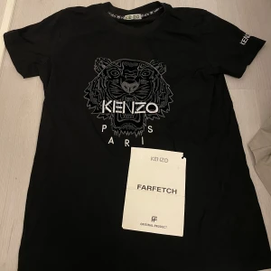  t-shirt från Kenzo med tigertryck - Snygg svart t-shirt från Kenzo med ett coolt tigertryck och texten 'Paris' på framsidan. T-shirten har korta ärmar och en rund halsringning. Perfekt för en stilren look.
