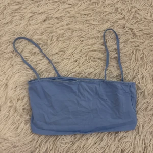 Blå tubtopp - Säljer en enkel blå tubtopp med smala axelband. Perfekt för varma sommardagar eller som ett lager under andra plagg.
