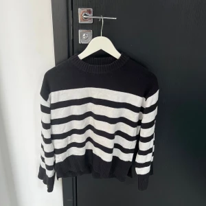 Svart och vit randig stickad tröja - Säljer en snygg svart och vit randig stickad tröja med rund hals. Tröjan har långa ärmar och ribbade kanter vid ärmslut och nederkant. Perfekt för en stilren look!