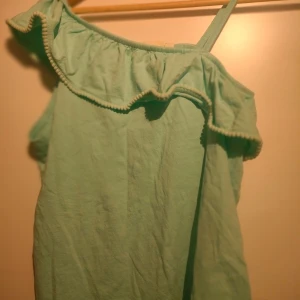 offshoulder topp med volang  - Säljer en söt mintgrön offshoulder topp med volang detaljer ifrån KappAhl. Toppen har en volangdetalj längs halsringningen och en axelbandslös design på ena sidan. Perfekt för varma sommardagar! Storlek 158/164 men passar mig som har XS/S.